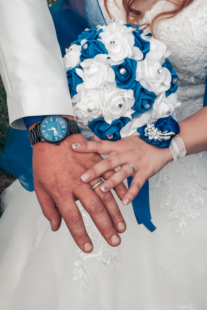 photographe de Joigny. photo Des alliances les mariés main dans la main, montrant leur alliances, et le bouquet de fleurs bleus et blanc. 89 Joigny.